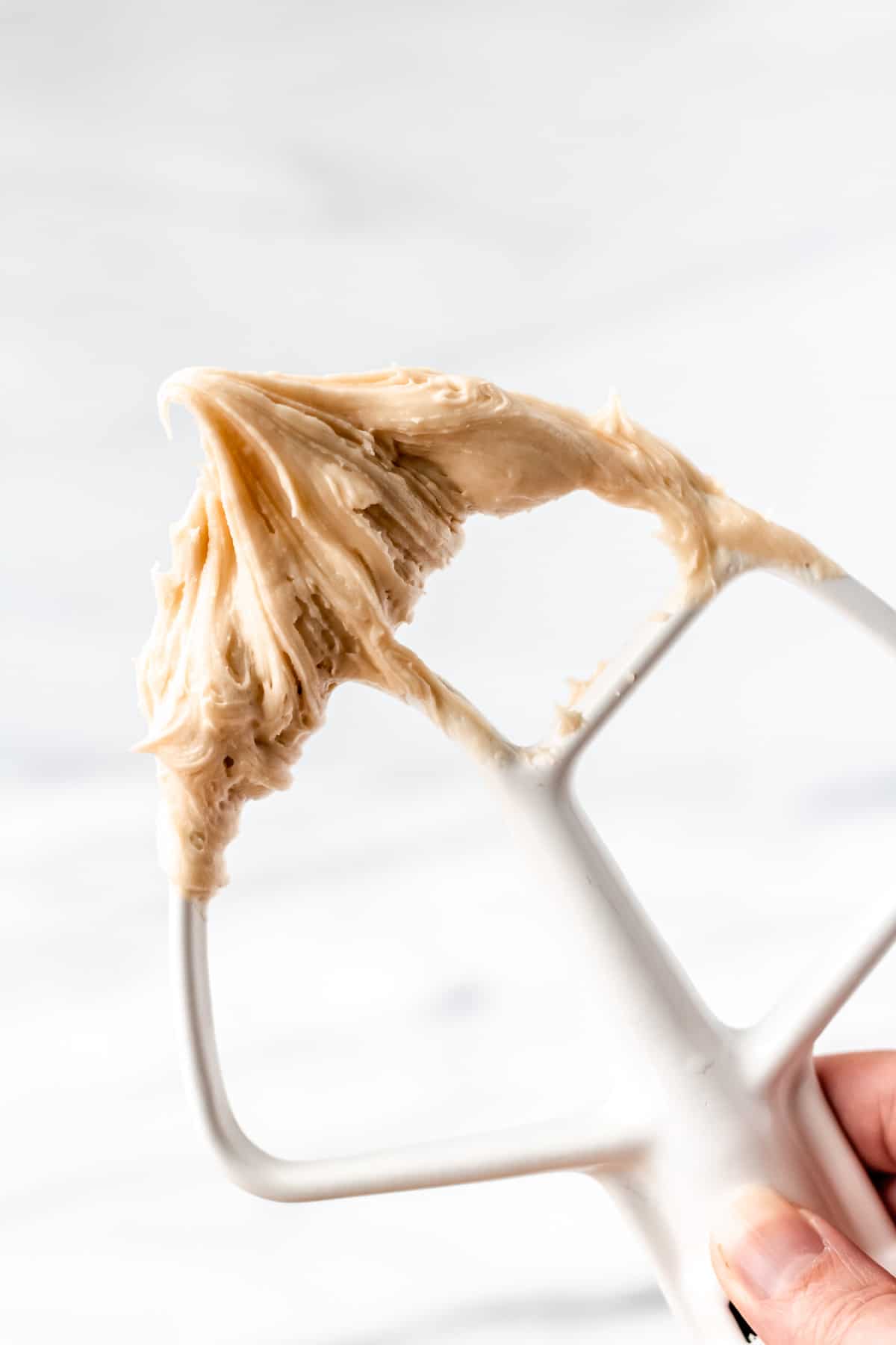 A hand holding up a paddle with caramel buttercream frosting on it.