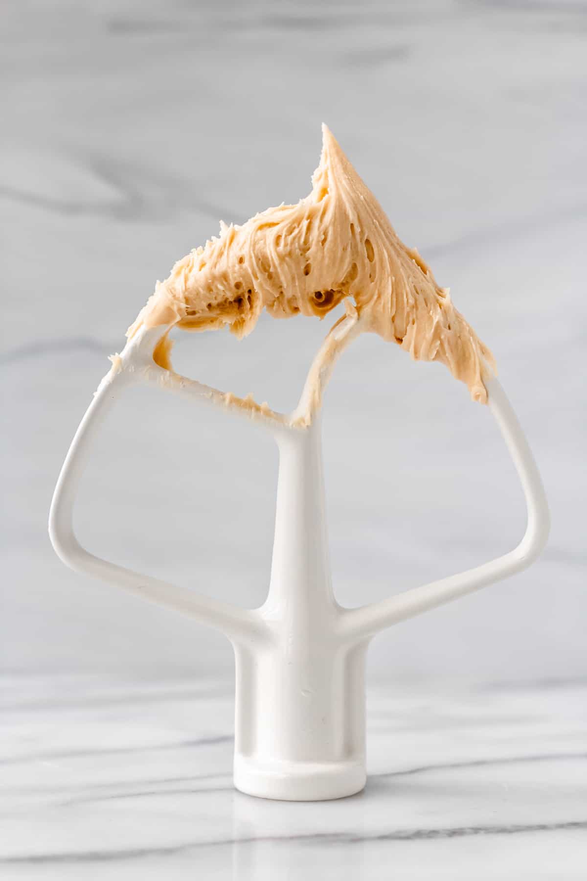 A paddle standing on a gray background with caramel buttercream frosting on it.