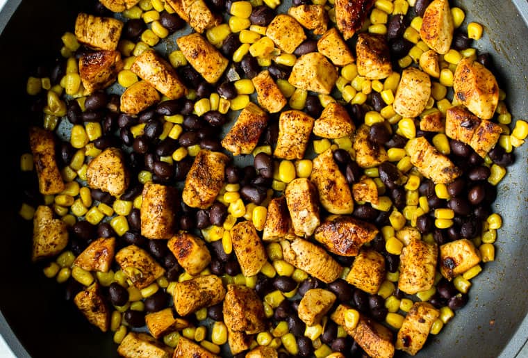 Chunks of chicken, corn, and black beans cooking in a black skillet