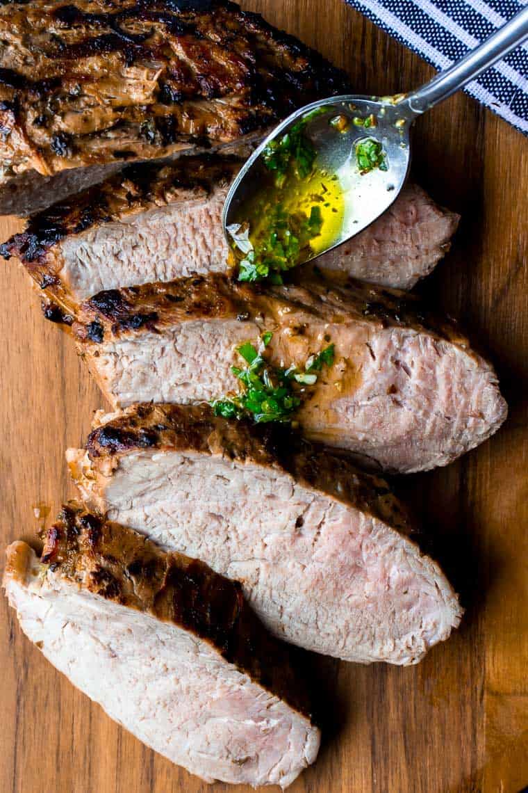 Spooning extra marinade over the roasted cuban pork tenderloin on a wood cutting board