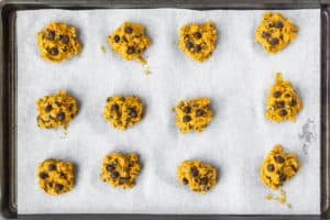 Pumpkin chocolate chip cookie dough spooned out onto a parchment paper lined baking sheet