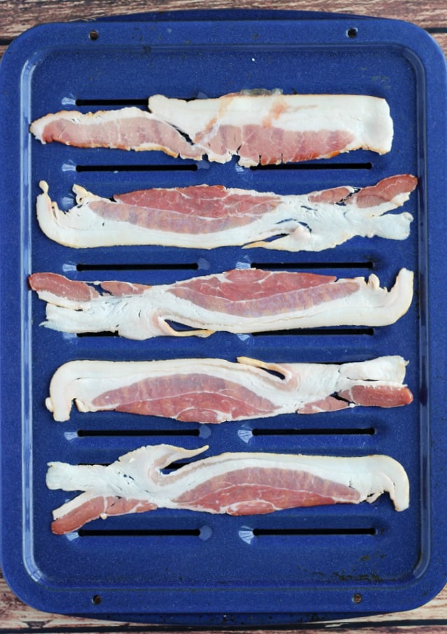 5 strips of bacon laid out on a blue broiler pan