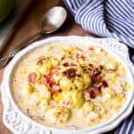 Cauliflower Corn Chowder in a white bowl over a wood board with a blue and white striped napkin and a spoon in the background