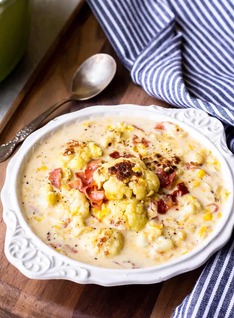 Cauliflower Corn Chowder in a white bowl over a wood board with a blue and white striped napkin and a spoon in the background