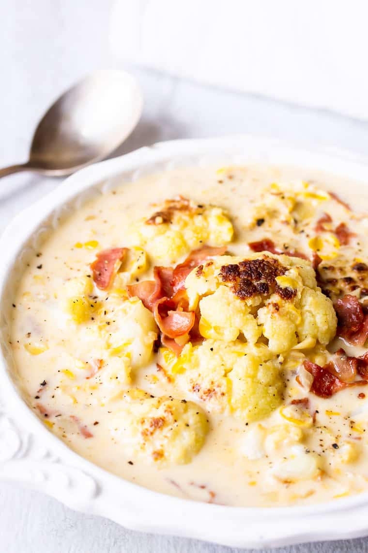 Cauliflower Corn Chowder in a white bowl over a white background with a spoon and a white napkin close by