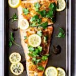 Baked Crispy Lemon Garlic Salmon on a baking sheet topped with fresh parsley and lemon slices with more lemon slices around it