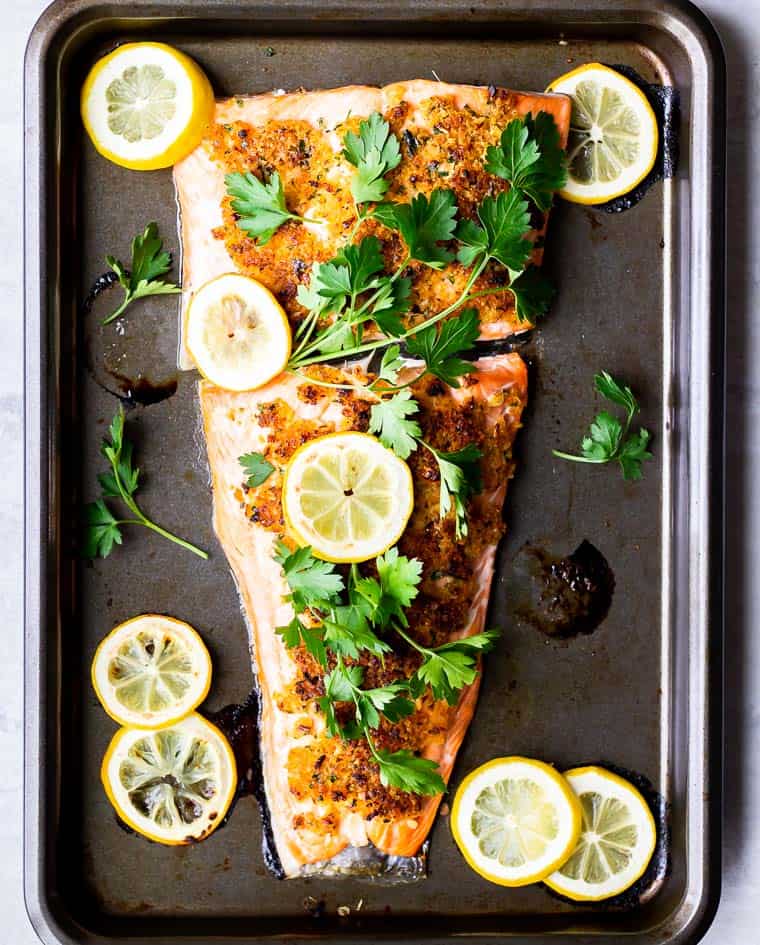 Baked Crispy Lemon Garlic Salmon on a baking sheet topped with fresh parsley and lemon slices with more lemon slices around it
