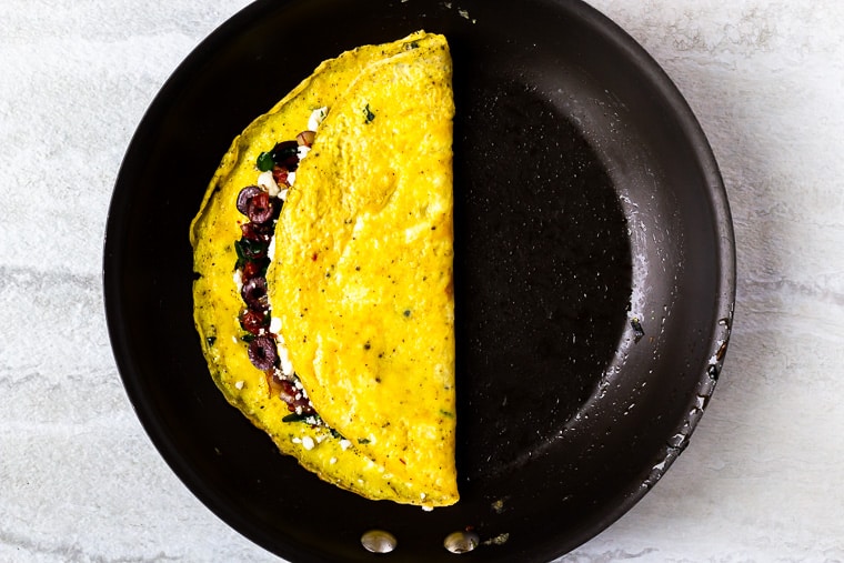 A Greek omelet folded in half in a black skillet over the white background