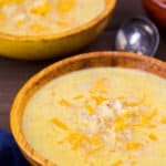 Low Carb Cheesy Cauliflower Soup in 2 Bowls with a spoon and blue napkin on a wood background