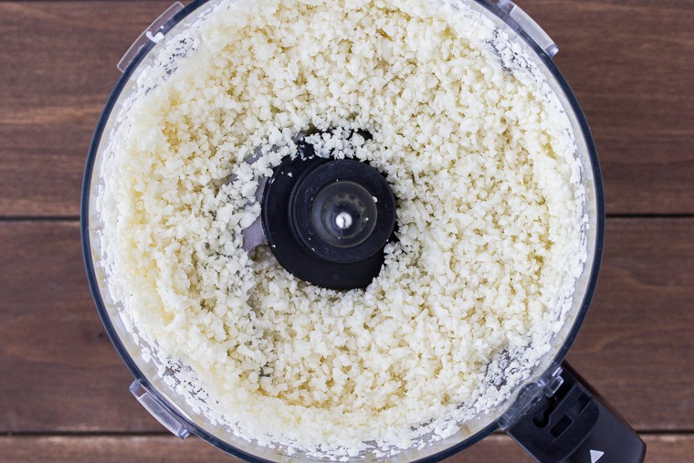 Riced Cauliflower in a Food Processor Bowl over a wood backdrop