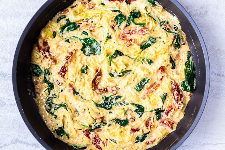 A black skillet with spaghetti squash, sun-dried tomatoes and spinach over a white background