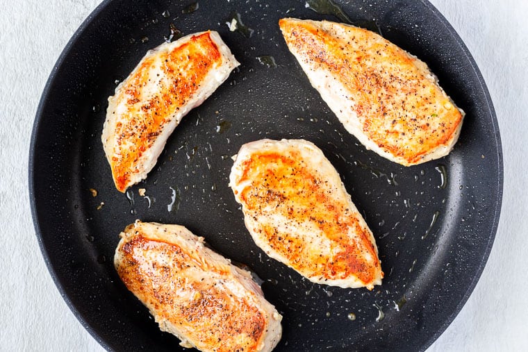 4 pan seared chicken breasts in a black skillet over a white background