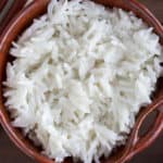 A brown bowl of coconut rice with chopsticks off to the side on a wood background