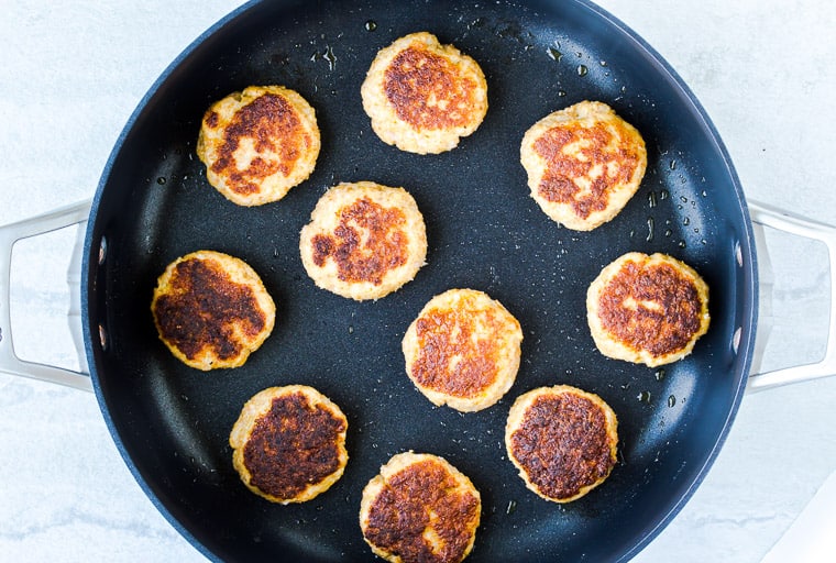 Fried shrimp cakes in a black skillet over a white background
