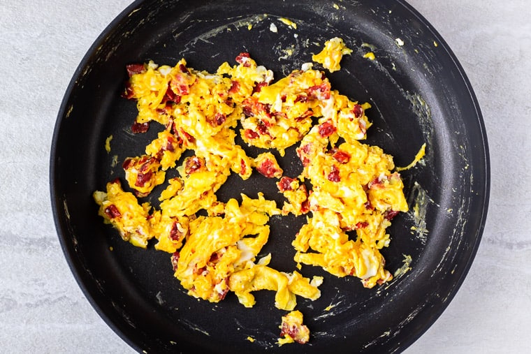 Scrambled eggs with bacon and cheese in a black skillet over a white background