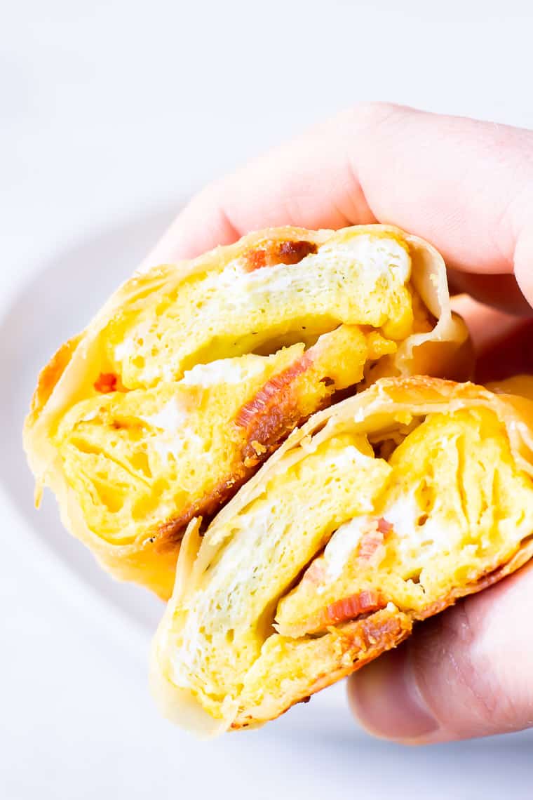 A hand holding 2 halves of a breakfast egg roll over a white background