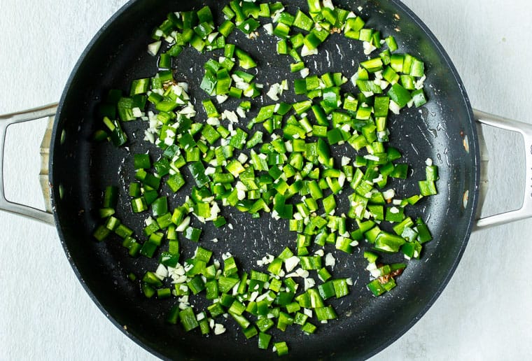 Diced jalapeno peppers and garlic cooking in a large, black skillet