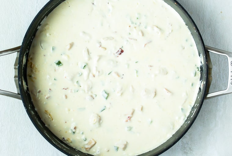 Cream cheese sauce with peppers and chicken in it in a large black skillet