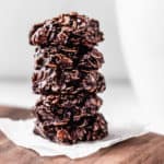 A stack of 5 Dark Chocolate No-Bake Cookies on a small piece of parchment paper on a wood board with a white mug in the background