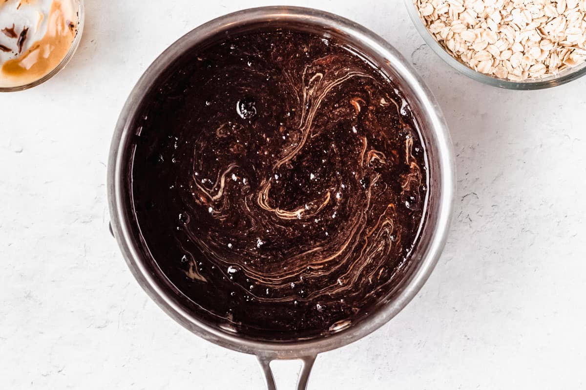 Chocolate mixture with peanut butter swirled into it in a saucepan on a white background with 2 bowls in the background