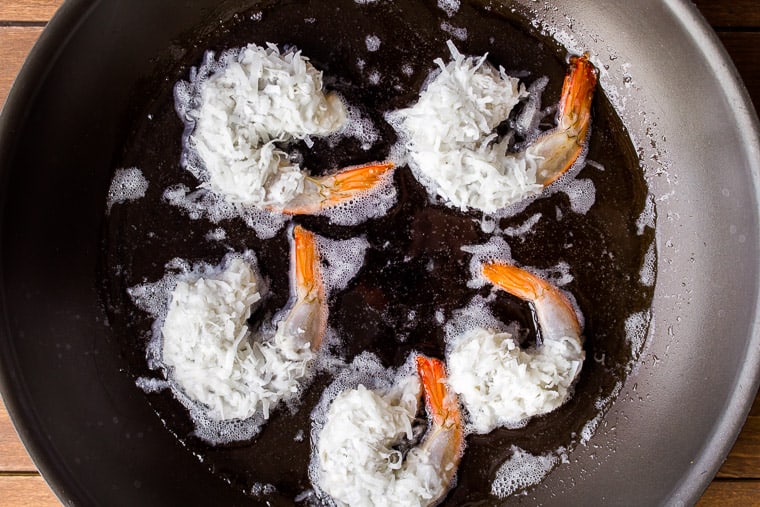 5 large coconut shrimp being fried in a black skillet