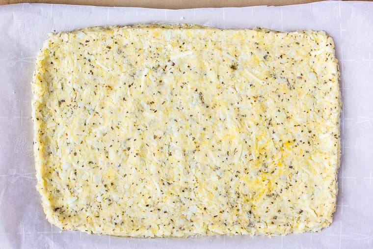 Cauliflower dough formed into a rectangular crust on parchment paper on a pizza stone