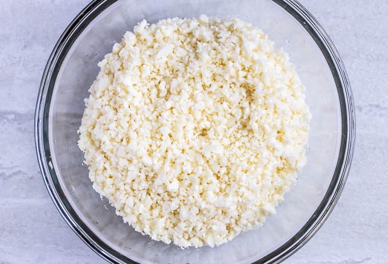 Riced cauliflower in a glass bowl over a white background