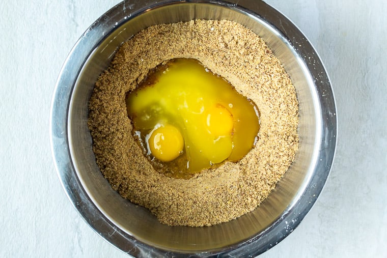 Flaxseed mixture with a well in the center filled with eggs, butter and vanilla extract in a silver bowl