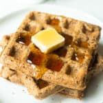 3 Flaxseed Waffles on a white plate with a white napkin and 2 white cups in the background