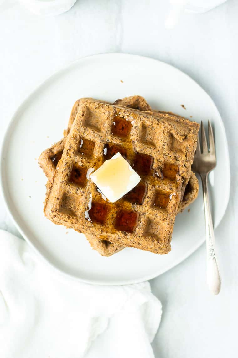 Overhead of Flaxseed waffles on a white plate with a fork and white napkin in the background