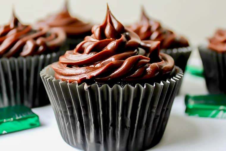 Close up of a Mint Chocolate Cupcakes with Chocolate Ganache frosting with more cupcakes and andes candies in the background