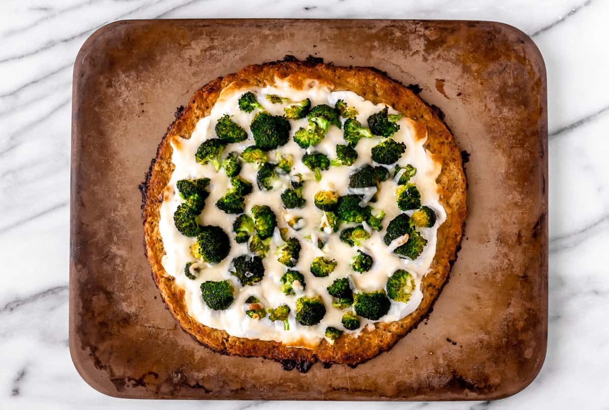 A baked ricotta pizza with broccoli on a pizza stone.