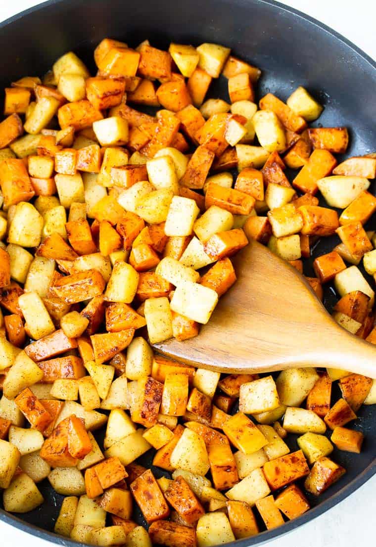 Sweet potatoes and apples in a black skillet with a wood turner