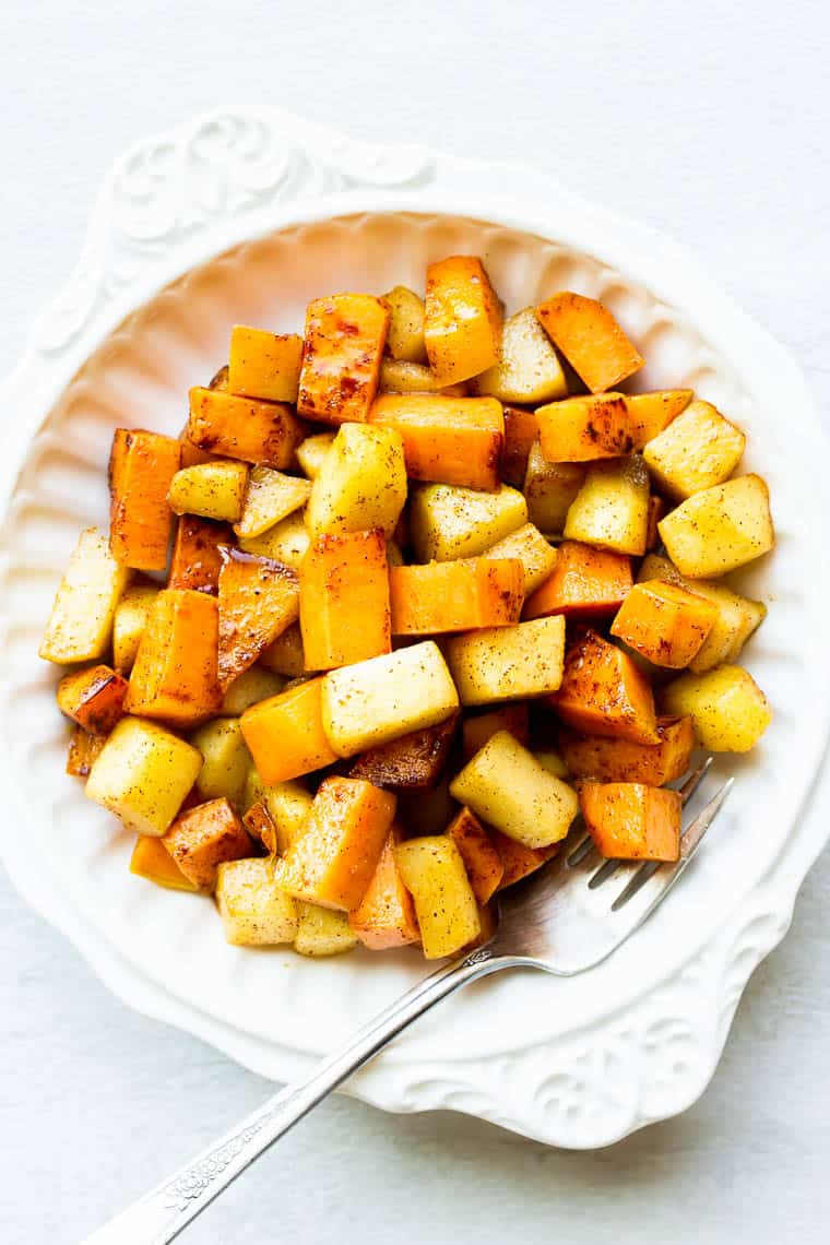 Maple Cinnamon Sweet Potatoes and Apples in a white bowl with a fork over a white background