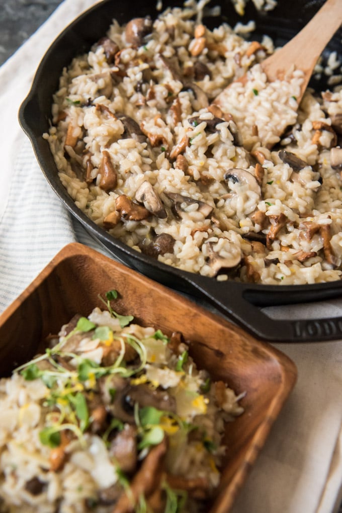 Mushroom Risotto in a cast iron skillet and a wood dish over a white background