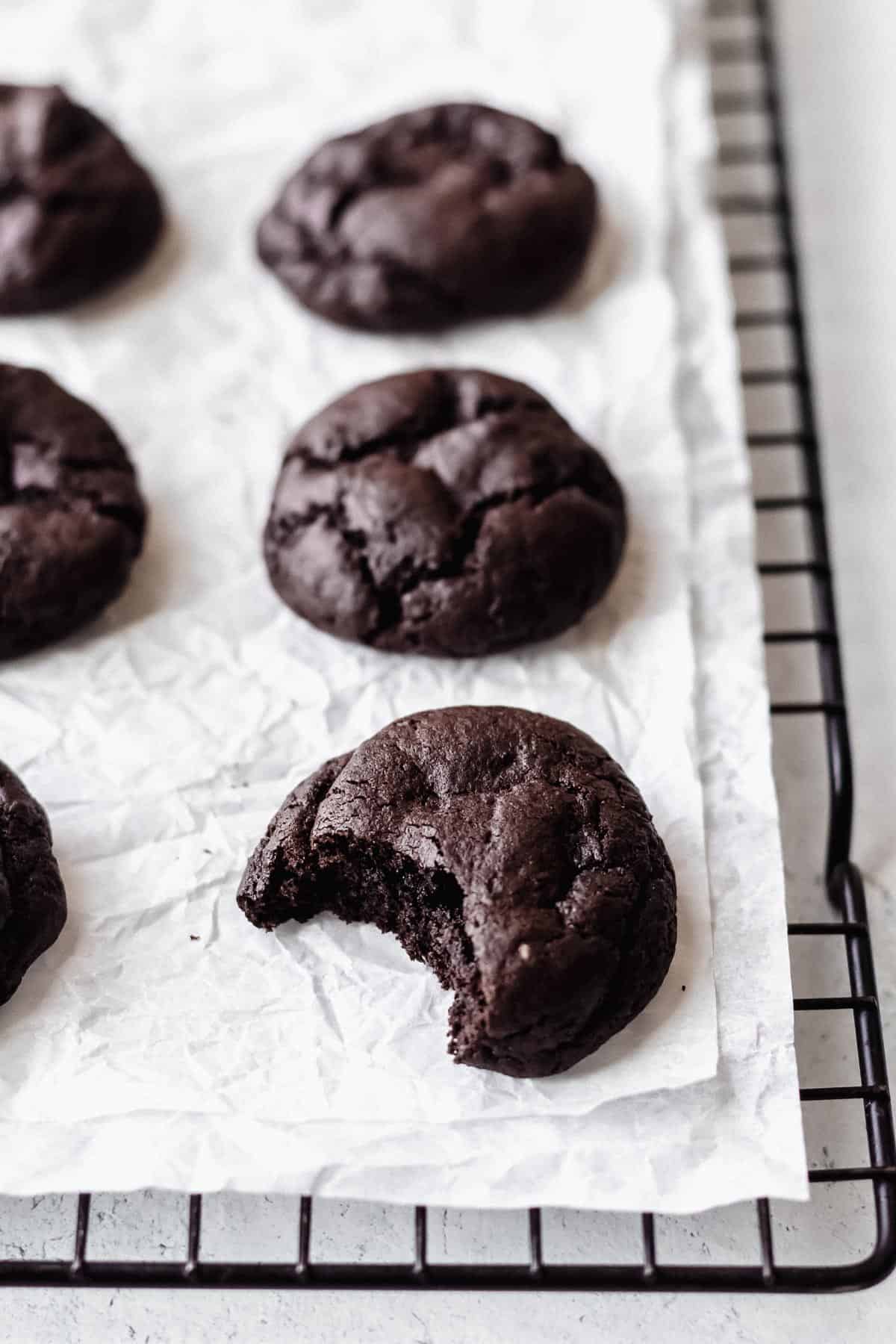 Dark chocolate cookies on a parchment paper lined cooling rack with a bite taken out of one of them