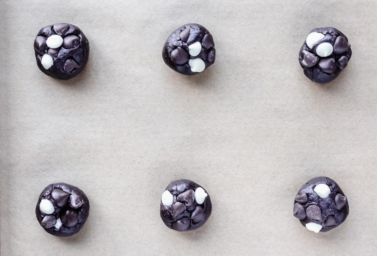 Triple dark chocolate chip cookie dough balls on a parchment paper lined baking sheet