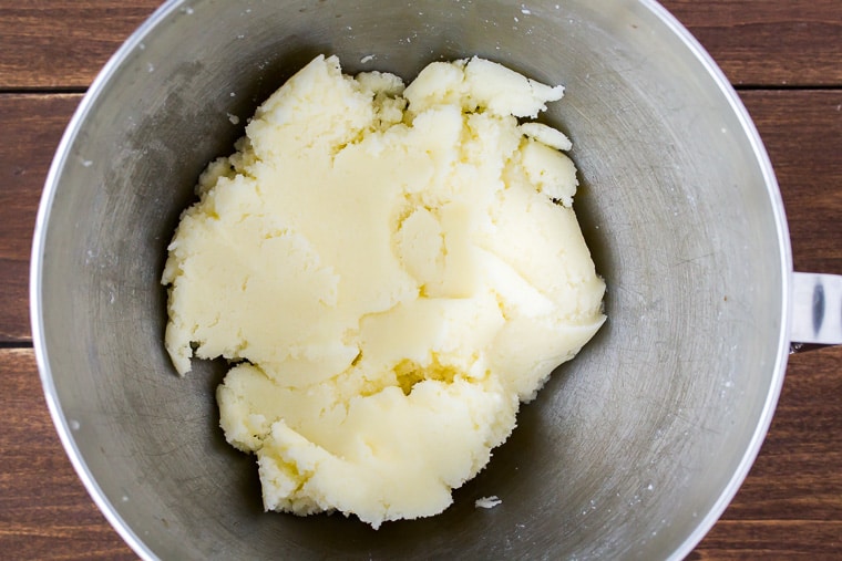 Butter and sugar creamed together until smooth in a silver mixing bowl on a wood background