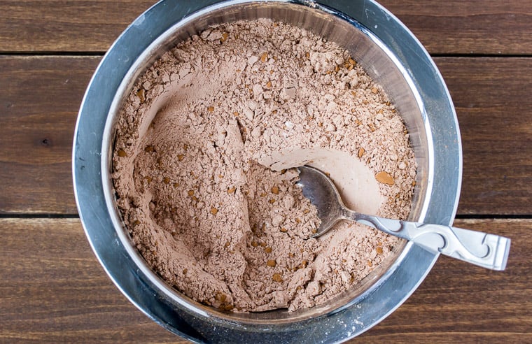 Dry ingredients for chocolate cookies in a silver bowl with a spoon on wood background