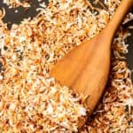 A close up of a wood spatula on a baking sheet with toasted coconut on it