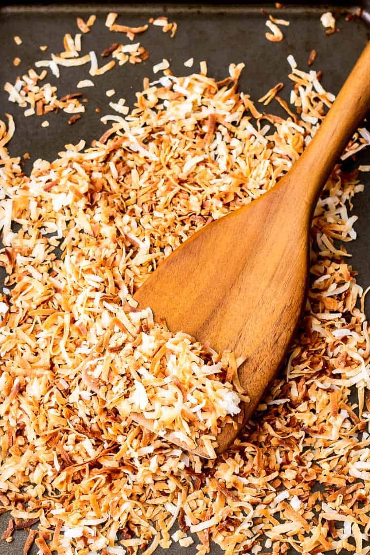 A close up of a wood spatula on a baking sheet with toasted coconut on it
