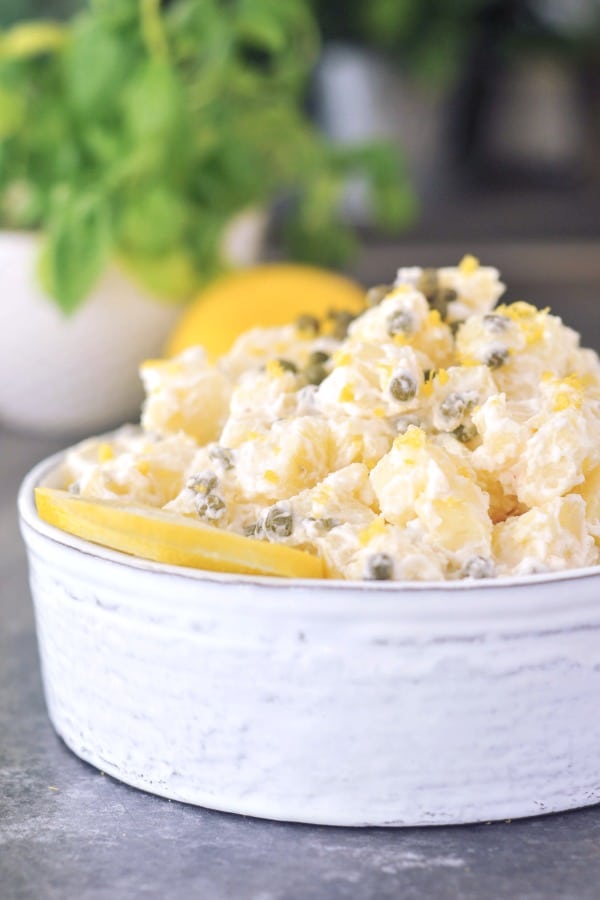 Lemon Piccata Potato Salad in a white bowl on a gray table with a plant in the background