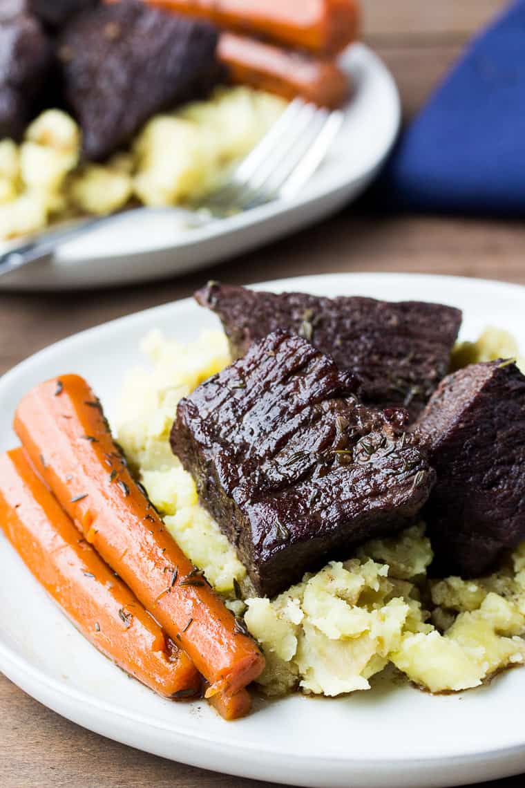 Red Wine Braised Short Ribs on White Plates with Mashed Potatoes and Carrots. All on a Wood Board with a Blue Napkin