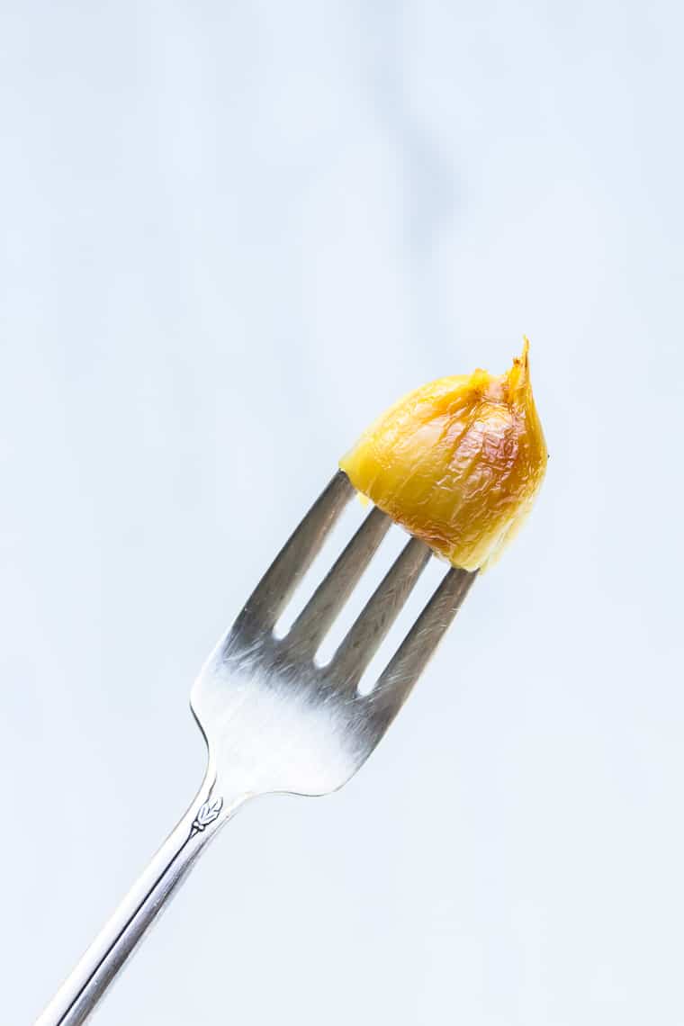 A fork holding a roasted garlic clove over a white background