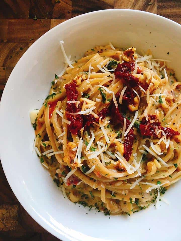 pasta with sun-dried tomatoes in a white bowl over a wood background