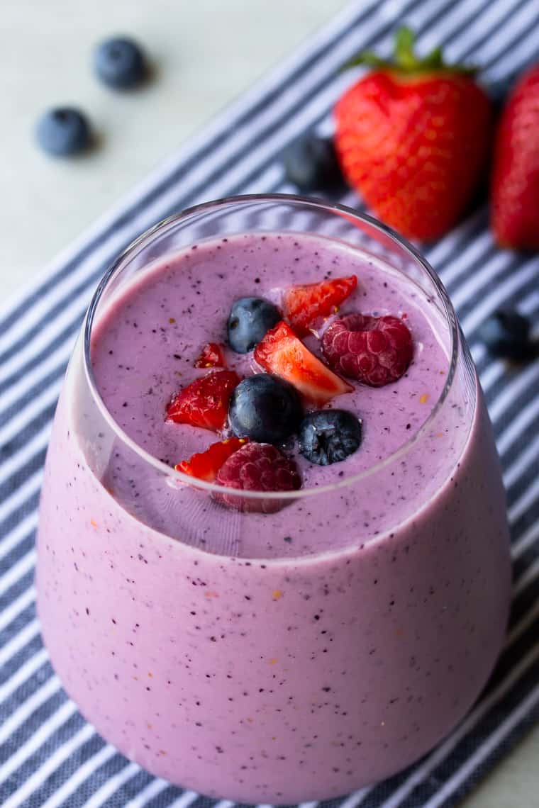 Mixed Berry Smoothie in a glass close up with strawberries and blueberries in the background