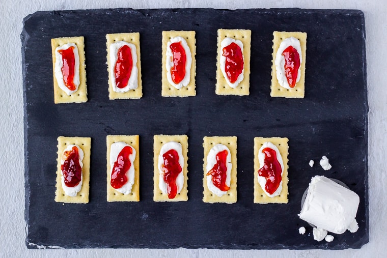 10 crackers topped with goat cheese and strawberry jam on a piece of slate