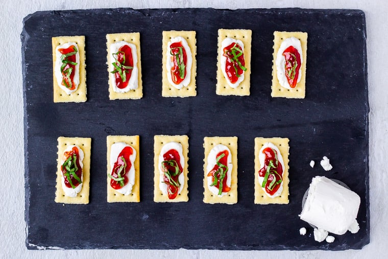 10 crackers on a piece of slate that are topped with strawberry jam and basil
