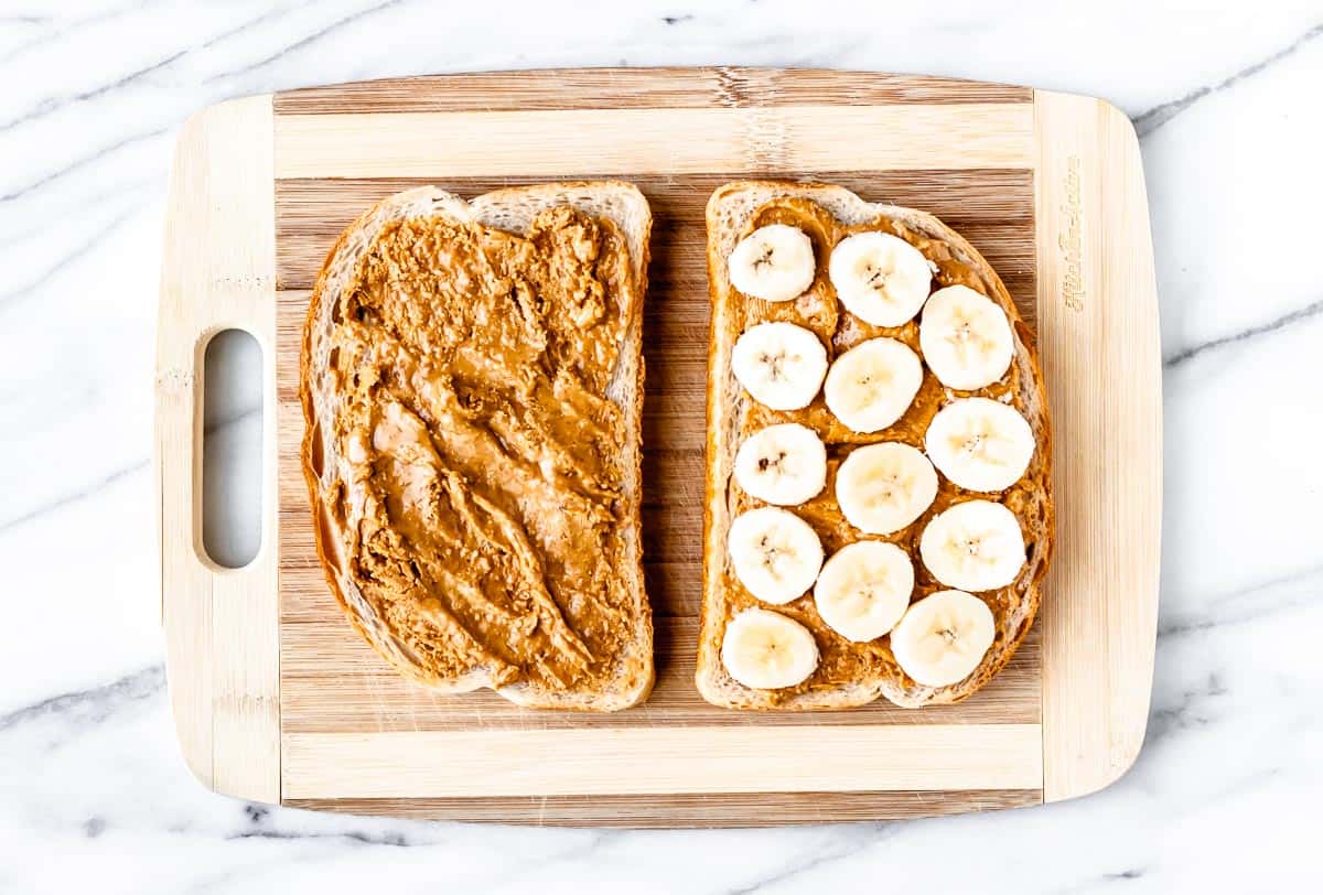 Two slices of bread spread with peanut butter with banana slices on one half.
