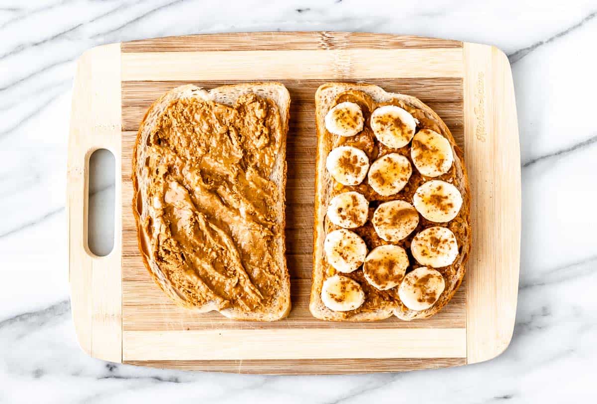 Two slices of bread spread with peanut butter with banana slices, cinnamon and honey on one slice.